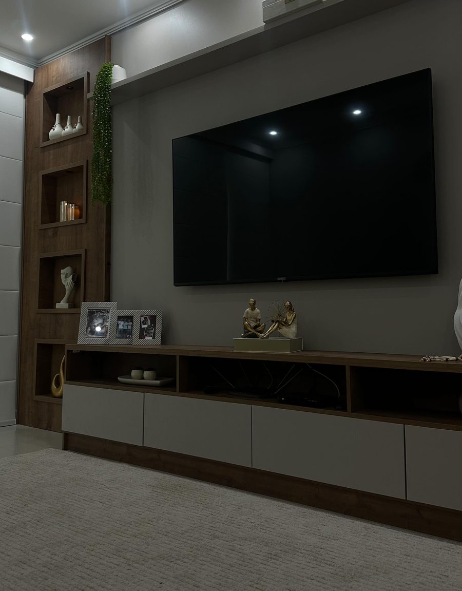 Sala com painel de madeira, televisão e nichos com objetos