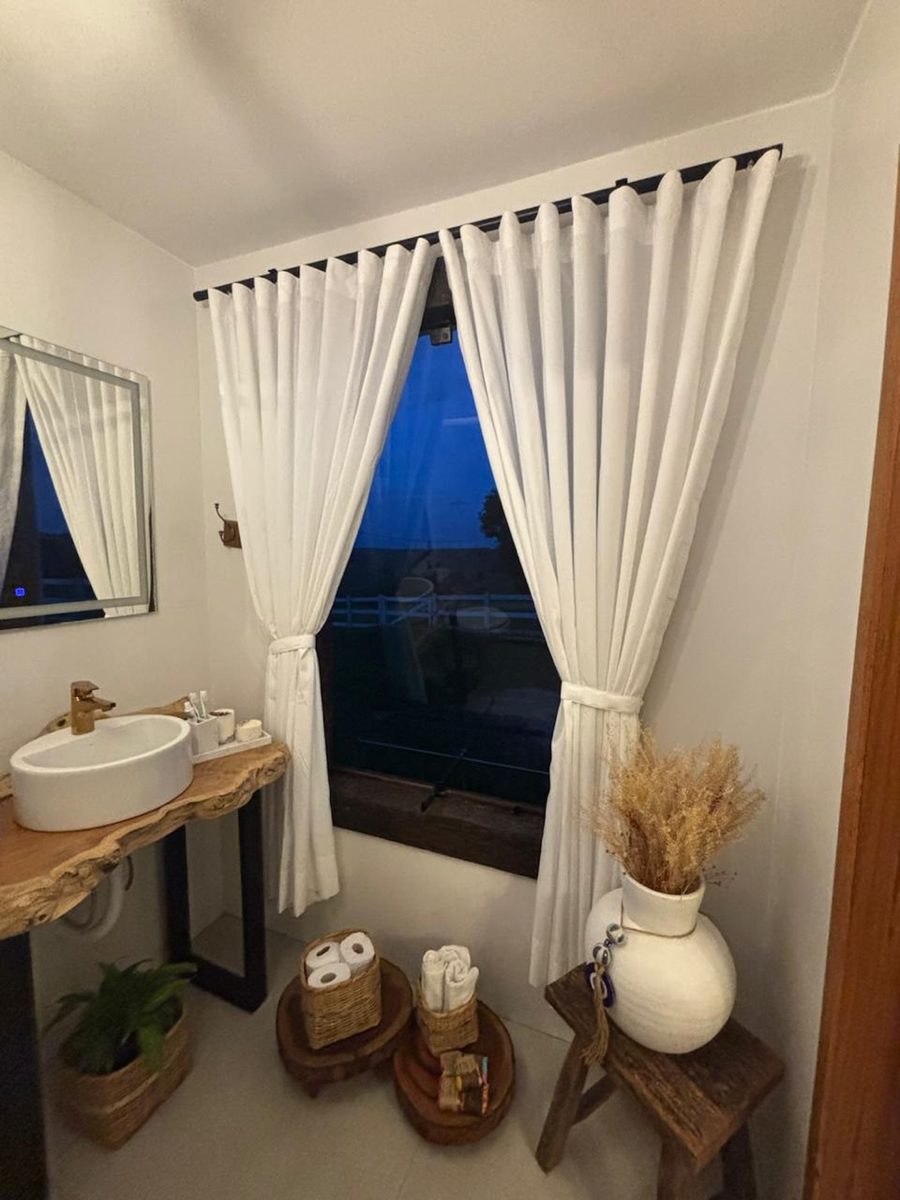 Cortinas brancas leves em uma janela, com bancada de madeira e vaso